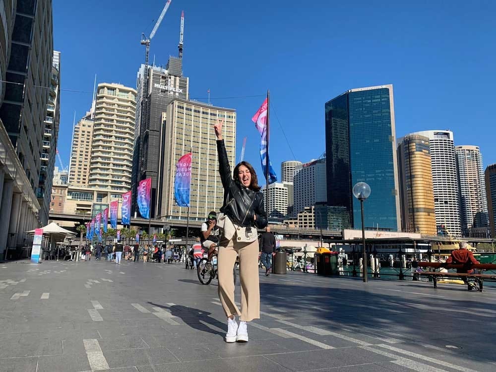 Dinero Australia chica morena con el brazo alzado y detrás los rascacielos de una ciudad